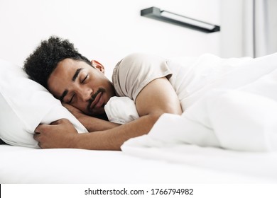 Photo of young african american man with mustache sleeping in white bed at bright room