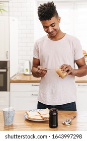 Photo of young african positive guy in the morning at the kitchen cooking breakfast make sweet jam sandwiches.