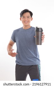 Photo Of A Young Asian Man With Muscular Body Holding A Shake Bottle Tumbler And Drink With One Hand Stand Facing On Isolated Background.