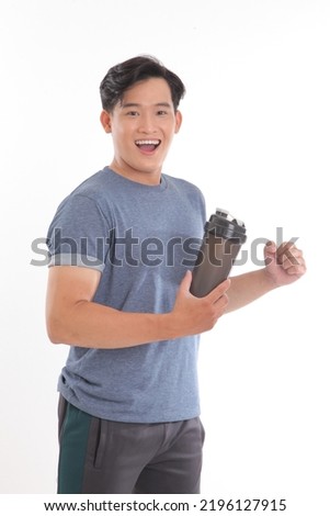 Photo of a young Asian man with muscular body holding a shake bottle tumbler and drink with one hand stand facing on isolated background.
