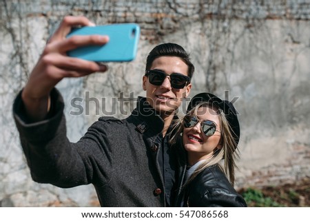 Photo of a young beautiful couple making selfie on wall background