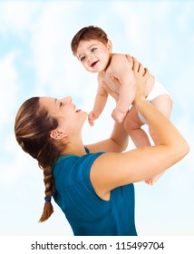 Photo Of Young Beautiful Mother With Cute Baby Boy, Smiling Mommy Lift Her Adorable Son, Pretty Woman Throwing Up Cheerful Little Child On Blue Sky Background, Happy Healthy Family, Love Concept