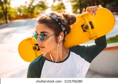 Photo of young beautiful woman walking outdoors with skateboard listening music with earphones. - Powered by Shutterstock