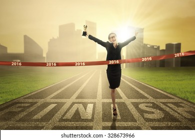 Photo Of Young Business Woman Winning The Race Competition And Crossing The Finish Line While Carrying A Trophy