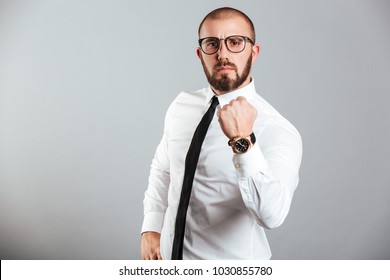 Photo of young businessman in white shirt and eyeglasses firmly showing fist meaning strength or fortitude isolated over gray background - Shutterstock ID 1030855780