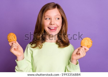 Photo of young cheerful girl happy positive smile lick tongue lips hungry delicious cookies isolated over violet color background