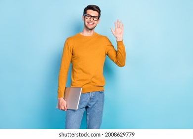 Photo of young cheerful man happy positive smile hold laptop waving hand hello isolated over blue color background