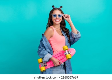 Photo of young cheerful pretty girl hold skateboard sportive eyewear isolated over turquoise color background