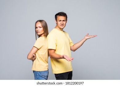 Photo Of Young Confused Loving Couple Gesturing With Hands Over Grey Wall And Looking At Each Other.