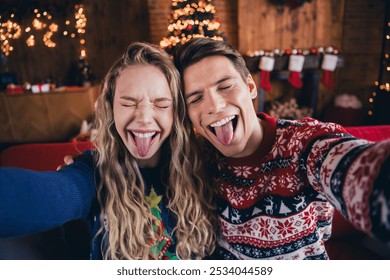 Photo of young couple take selfie photo stick tongue out wear christmas clothes enjoy cozy x-mas party decoration interior flat indoors - Powered by Shutterstock