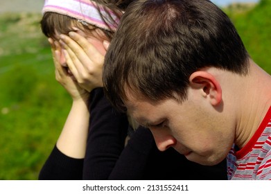 Photo Of A Young Couple Unhappy Sad Negative Disagreements, Conflicts, Morose, Bad Problems, Bored, Sitting On A Field In The Mountains 