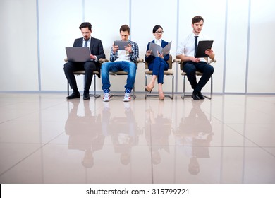 Photo Of Young Creative Business Team Of Four With Documents And Computers. They Sitting In A Row And Working. One Man Wearing Informal Clothes