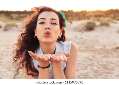 Photo of young cute caucasian lady looking at camera on the beach blowing kisses.