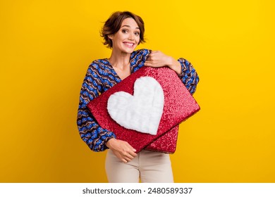 Photo of young cute lady wearing vintage blouse hugging her one gift from boyfriend huge heart pillow isolated on yellow color background - Powered by Shutterstock