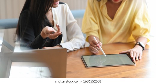 Photo of young designer team discussing/meeting/talking about their business by using a computer tablet and laptop while sitting together at the wooden table over orderly living room as background.