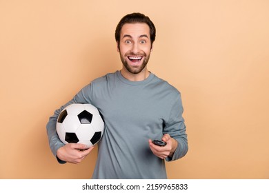 Photo Of Young Excited Guy Holding Ball Watching Football Match Tv Weekend Isolated Over Beige Color Background