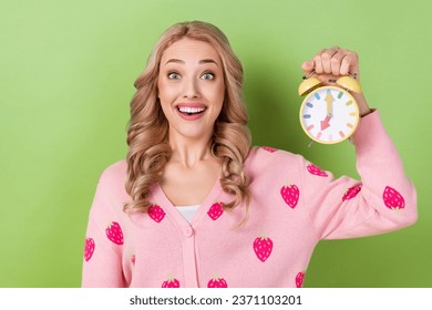 Photo of young funny girl blonde curly hair wear jumper strawberry print hold morning timer ring awake isolated on green color background