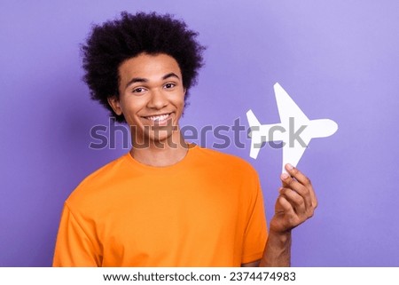 Photo of young funny guy wear orange t shirt stylish hold paper origami airplane cheap tickets flight isolated on violet color background