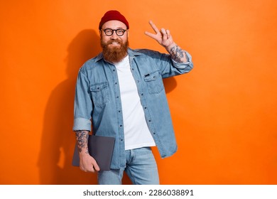 Photo of young guy working project team leader show v-sign successful it engineer hold netbook casual outfit isolated on orange color background