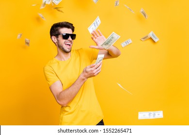 Photo of young handsome careless guy throwing money banknotes away wealthy person wear sun specs casual t-shirt isolated bright yellow color background