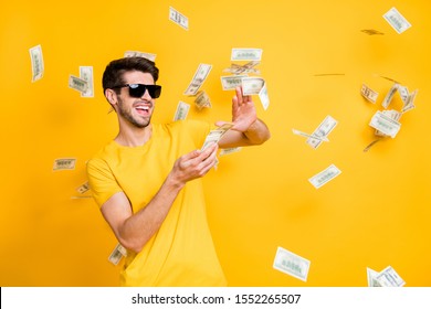 Photo of young handsome careless guy throwing usa money banknotes away wealthy person wear sun specs casual t-shirt isolated bright yellow color background