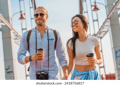 Photo of young happy couple at street walking drinking coffee and talking with each other, spending time together while traveling, sightseeing exploring the city - Powered by Shutterstock