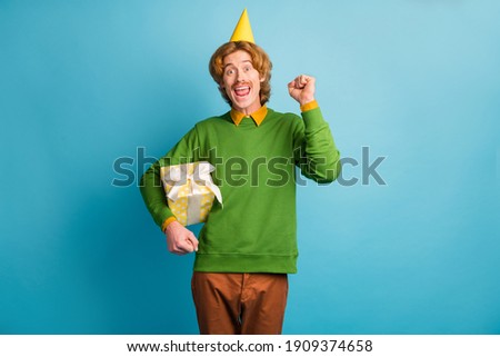 Photo of young happy excited smiling cheerful man with cone on head hold birthday gift isolated on blue color background