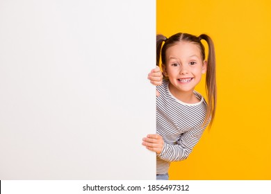 Photo of young happy smiling little girl child kid stand behind white wall isolated on yellow color background