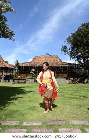 photo of a young Javanese girl practicing dancing in the front yard of a house with a traditional Javanese design
