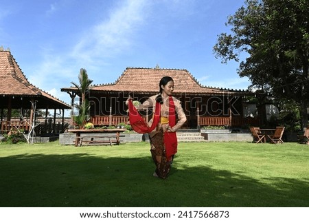 photo of a young Javanese girl practicing dancing in the front yard of a house with a traditional Javanese design

