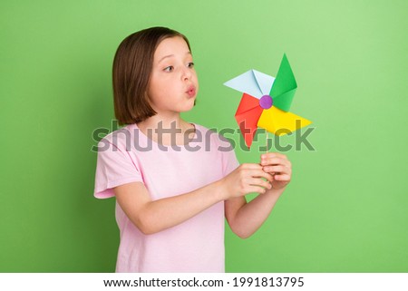 Photo of young little girl blow windmill pinwheel rotate toy isolated over green color background