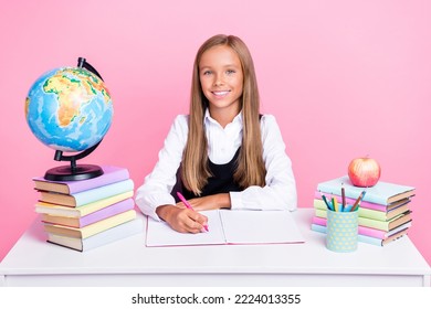 Photo Of Young Little Preteen Schoolgirl Sitting Desk Writing Copybook Toothy Smile Books Decoration Globe Isolated On Bright Pink Color Background