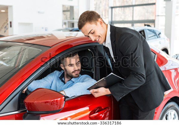 Photo of young male\
consultant and buyer signing contract for new car in auto show.\
Concept for car rental