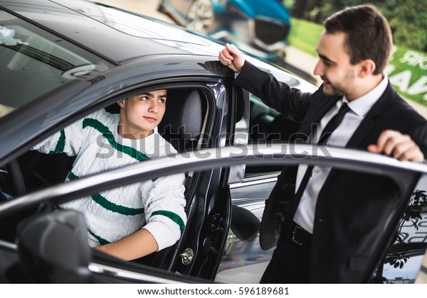 Photo of young male consultant and buyer\
in new car in auto show. Concept for car\
rental