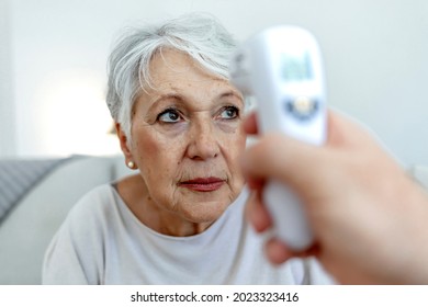 Photo of a young male doctor testing senior woman for temperature with an infrared thermometer at home. Healthcare worker at home visit. Female doctor is checking temperature to senior woman. - Powered by Shutterstock