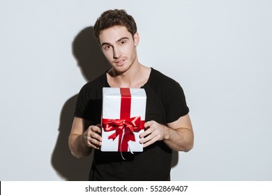 Photo Of Young Man Dressed In Black T-shirt Standing Over White Background Holding Gift.