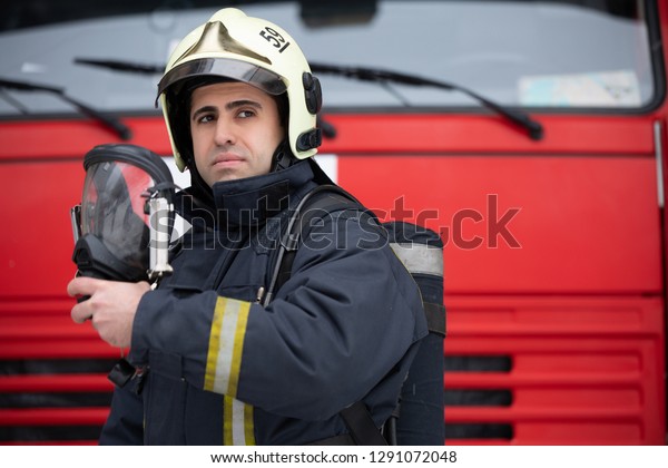 Photo of young man fireman with mask in hands near\
fire truck