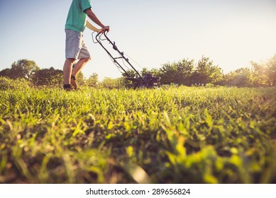Photo of a young man mowing the grass during the beautiful evening.