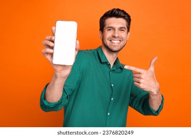 Photo of young man student wear green shirt point finger smartphone gadget modern app display web store isolated on orange color background