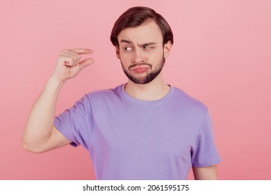 Photo of young man unhappy sad upset show tiny small size measures with fingers dislike isolated over pink color background