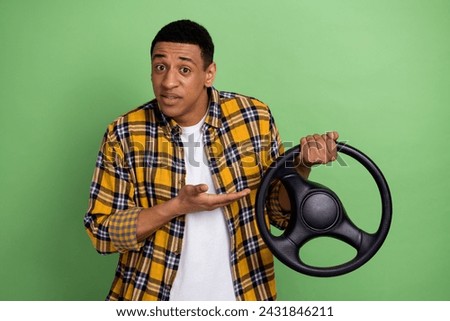 Photo of young man wearing yellow stylish checkered shirt demonstrate volkswagen auto steering wheel isolated on green color background