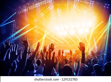 Photo of young people having fun at rock concert, active lifestyle, fans applauding to famous music band, nightlife, DJ on the stage in the club, crowd dancing on dance-floor, night performance
