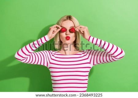 Photo of young positive woman blonde hair striped stylish top kiss red lipstick cover eyes strawberries isolated on green color background