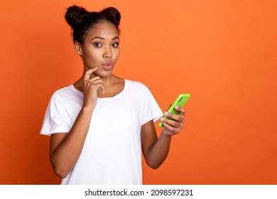 Photo of young pretty african lady finger touch chin use smartphone minded isolated over orange color background