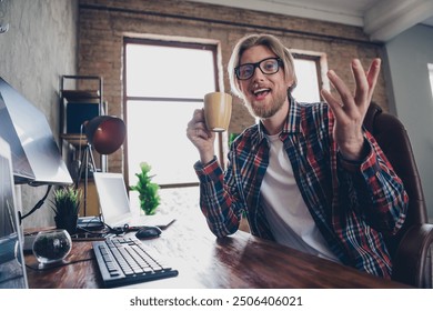 Photo of young project manager man blond hair wear plaid shirt sitting workplace using computer having video conference drinking tea - Powered by Shutterstock