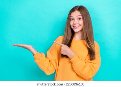 Photo of young satisfied pretty teenager lady wear orange sweater hold palm finger point mockup new college opening isolated on cyan color background - Powered by Shutterstock