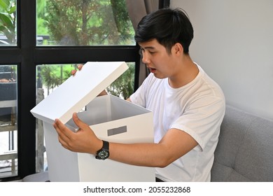 Photo Of Young Smart Man Unwrapping A White Box With The Comfortable Sitting Room As A Background.