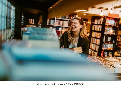 Photo Of Young Smiling Woman Sorting Books To The Book Shelves. Young Woman Enjoying Her Part Time Job At Bookstore Because She Is Book Lover.