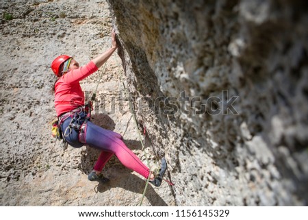 Photo of young sports woman in red helmet looking up climbing on mountain