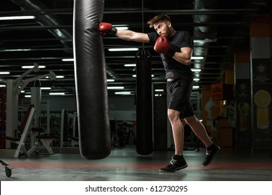 Фотография молодого сильного спортсмена, боксера, выполняющего упражнения в тренажерном зале и смотрящего в сторону.